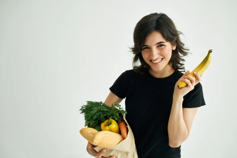 Весёлая брюнетка с пакетом овощей, доставка продуктов