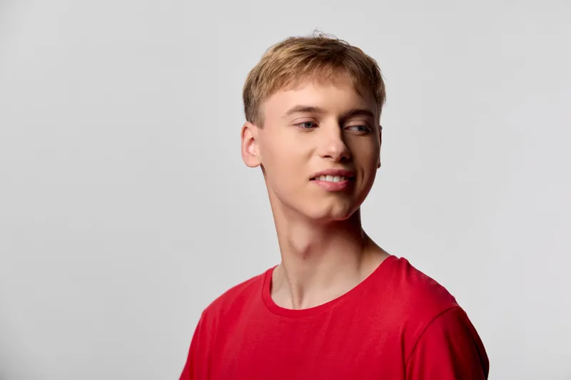 Male in a casual redshirt gazes to the side with a smiling expression against a neutral studio background, clean lighting and modern styling for fashion and lifestyle projects