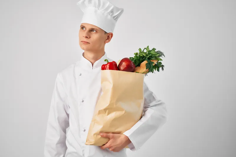 Мужчина в поварской форме с пакетом продуктов