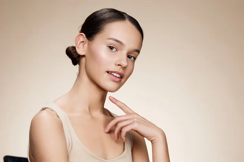 Young woman with natural beauty and soft smile, showcasing skincare routine on neutral background, exuding confidence and serenity in a minimalist style