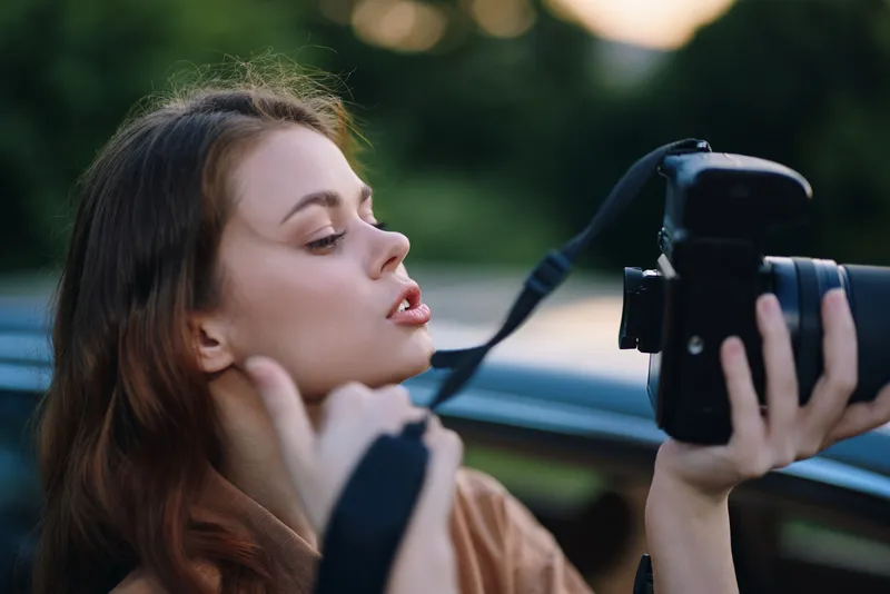 Young woman capturing professional photography with a camera, showcasing creativity and passion against a blurred outdoor background during golden hour.