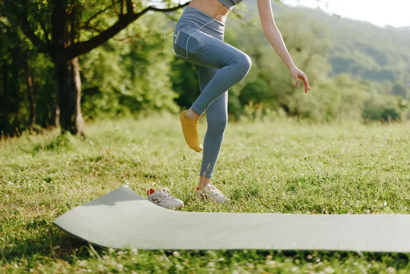 Young woman practicing yoga outdoors on a green mat, embodying health, balance, and tranquility in a serene natural setting