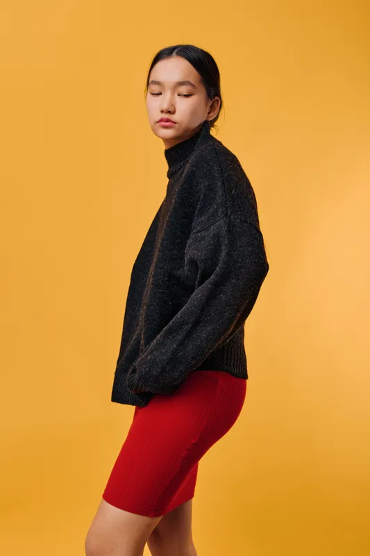 Young woman posing with closed eyes in black sweater and red skirt against yellow background. Fashion, portrait, casual style and serene mood in studio with simple setup and warm colors.