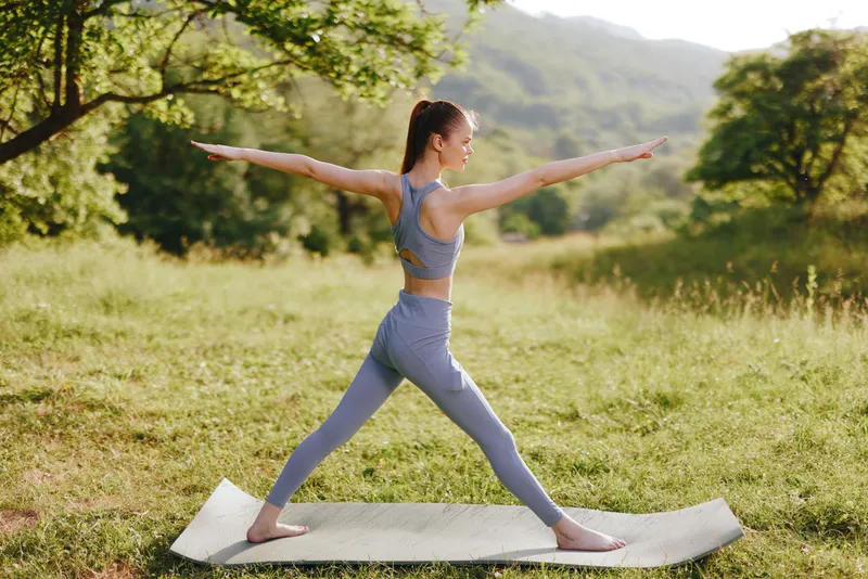 Young woman practicing yoga outdoors in a natural setting, wearing comfortable activewear in soft colors, promoting relaxation and wellness