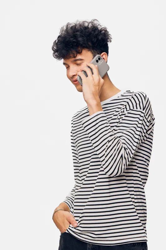 young man talking on smartphone wearing striped long sleeve shirt, casual style, curly hair, isolated on white background, modern communication technology