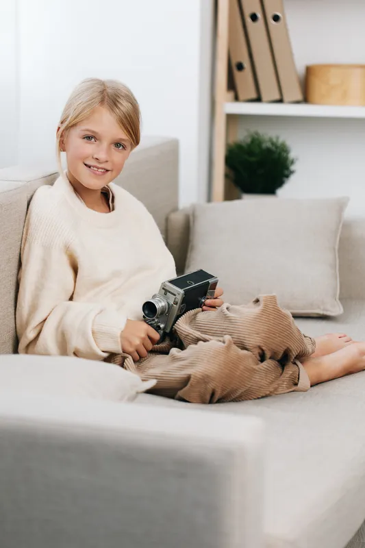 Authentic play scene featuring a young girl at home, using a toy camera to imagine school days, routines, and everyday lifestyle in a cozy, candid setting.