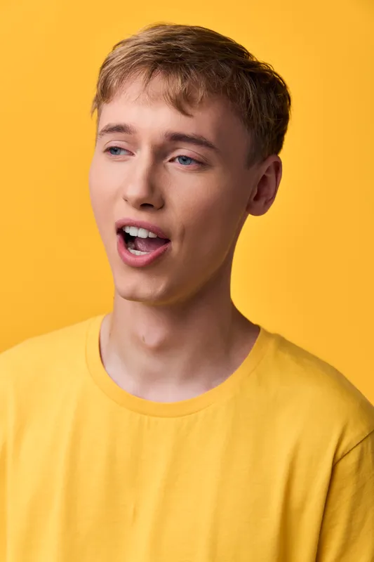 Young man in a yellow shirt sings with open mouth against a bright backdrop, conveying energy and expression for advertising, media, and creative projects with impact