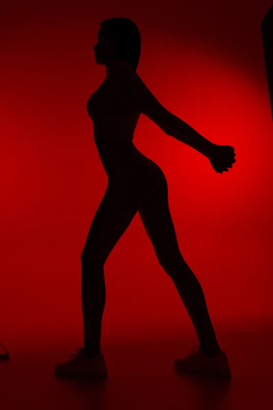 Silhouette of a woman sport fitness workout in dynamic pose, stretching her arms against vivid red background, showing strength and flexibility.