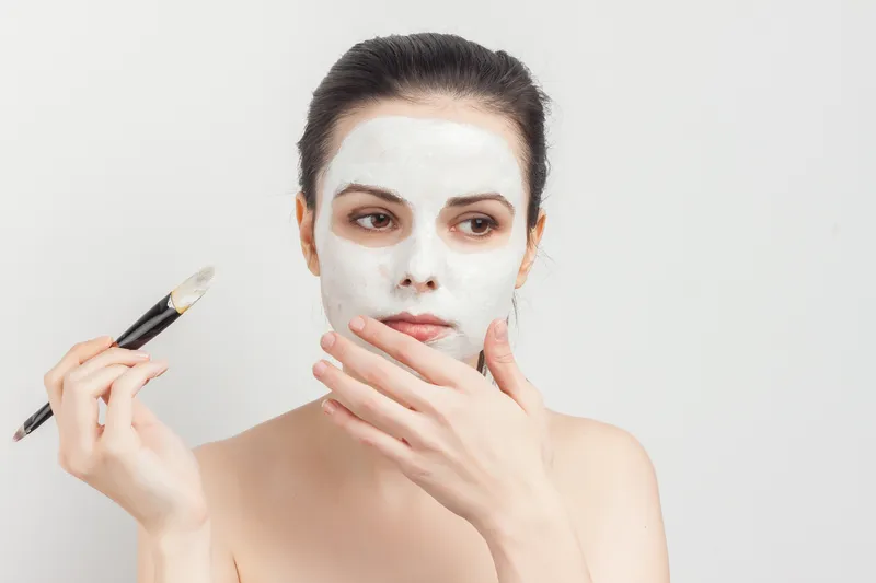 Брюнетка с кремовой маской для лица, уход за кожей, кисть для нанесения макияжа