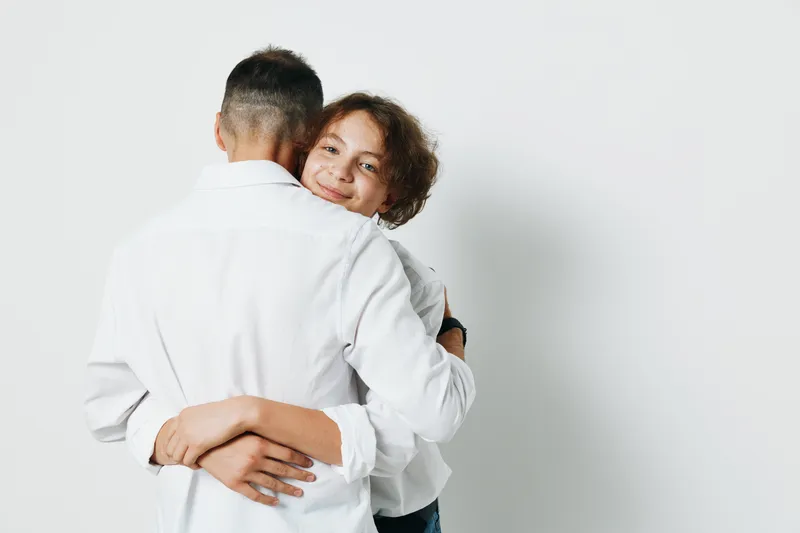 A business professional man hugs a colleague against a solid colored background, radiating warmth, trust, and relief in a moment of team support.