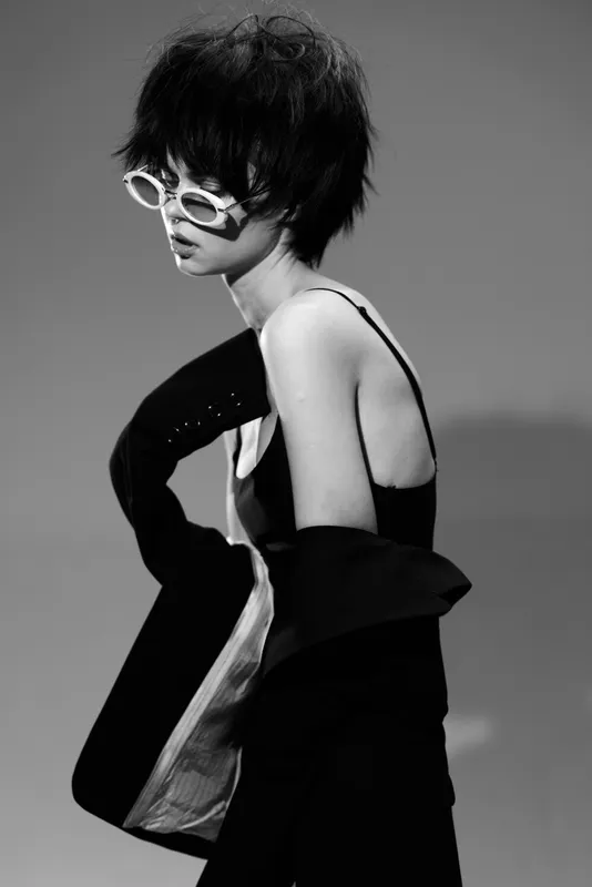Stylish woman wearing sunglasses and a trendy black outfit in black and white.