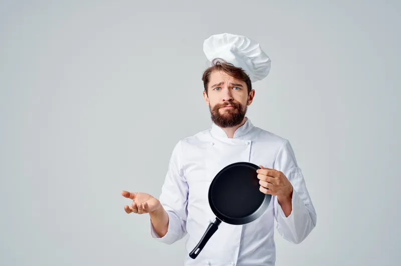 Бородатый мужчина-шеф-повар готовит на сковороде на кухне, представляя кулинарную индустрию