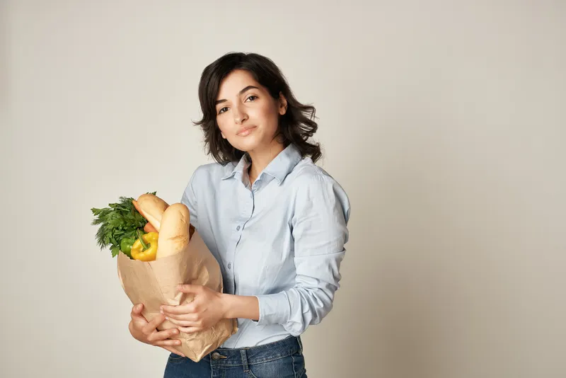 Брюнетка с пакетом продуктов из супермаркета, доставка диетического питания на тёмном фоне