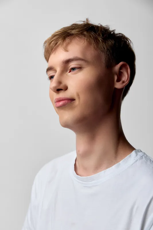 Young man in a white t shirt with a calm profile and subtle studio lighting, capturing a thoughtful mood and relaxed pose for lifestyle or fashion use.