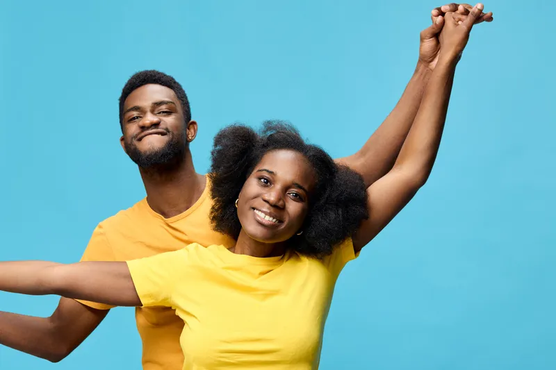Happy young African American couple enjoying their time together in vibrant yellow and orange t shirts against a bright blue background, expressing joy and connection