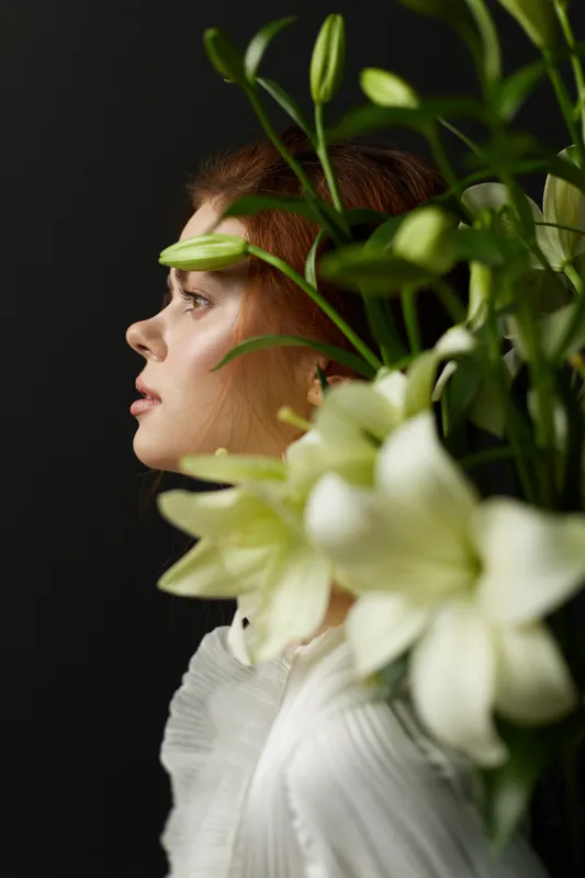 Profile of a beautiful young woman with long hair surrounded by white flowers, showcasing elegance, grace, and tranquility in a dark background