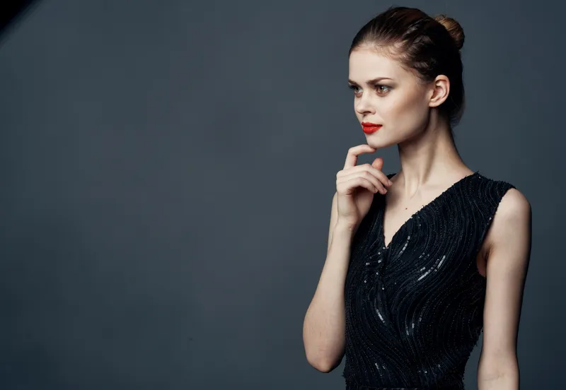 Женщина в черном платье с обнаженными плечами на сером фоне