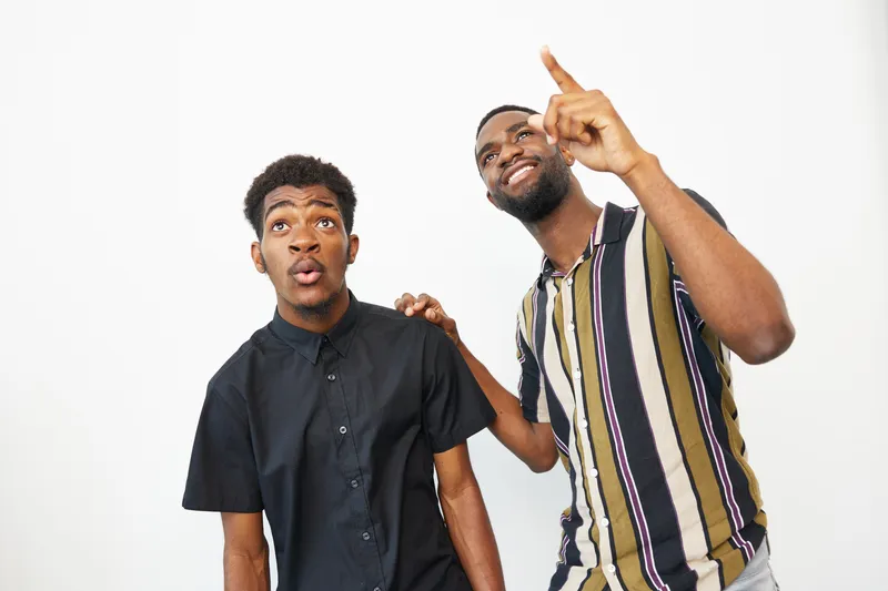 Two African American men expressing surprise and excitement, showcasing a vibrant moment with dynamic emotions and casual attire, perfect for lifestyle themes.
