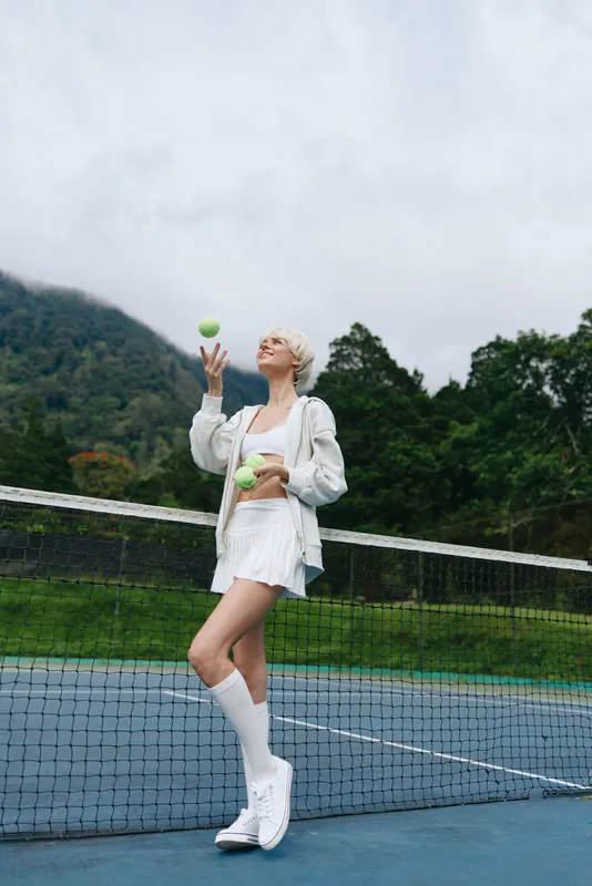 Young athletic woman juggling tennis balls on a court in sporty outfit with a natural green background showcasing active lifestyle and joy