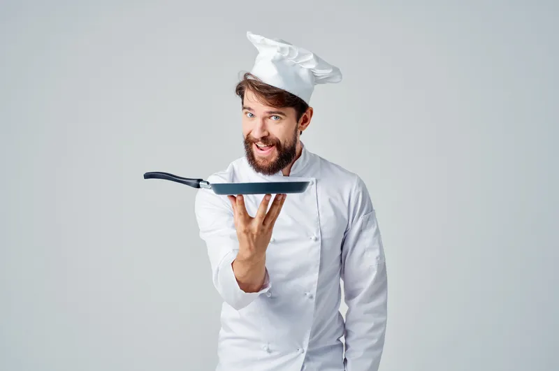 Мужчина в поварской форме с кухонными принадлежностями, работа, светлый фон