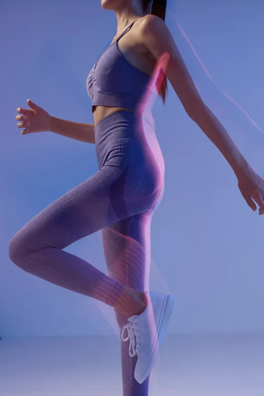 Woman sport fitness in purple activewear performing dynamic workout with modern pink light trails on blue studio background, showcasing strength and motion.