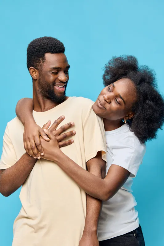 Happy young couple sharing a joyful moment, wearing casual pastel shirts, against a vibrant blue background, showcasing love and connection