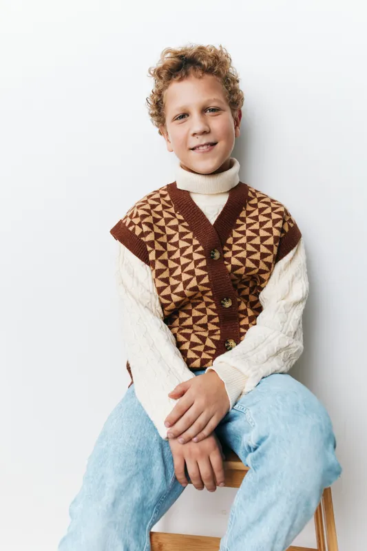 Authentic portrait of a school aged boy in a patterned knit vest and cozy sweater, captured in a simple lifestyle pose that emphasizes warmth and realism.