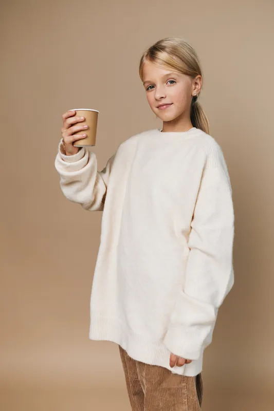 Authentic scene of a young girl in a cozy oversized sweater holding a paper cup, capturing a simple lifestyle moment tied to school and everyday play.