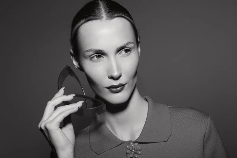 White woman with pale skin holds broken mirror piece near face in black and white studio portrait concept for reflection and identity.