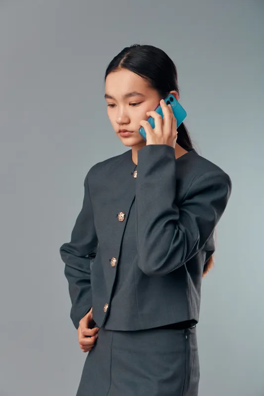 Young woman in business suit talking on smartphone with serious expression isolated on light background. Asian female professional discussing work or communication on mobile device.