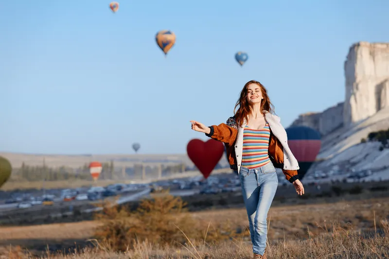 Яркие воздушные шары парят позади стильной женщины в полосатой рубашке и джинсах
