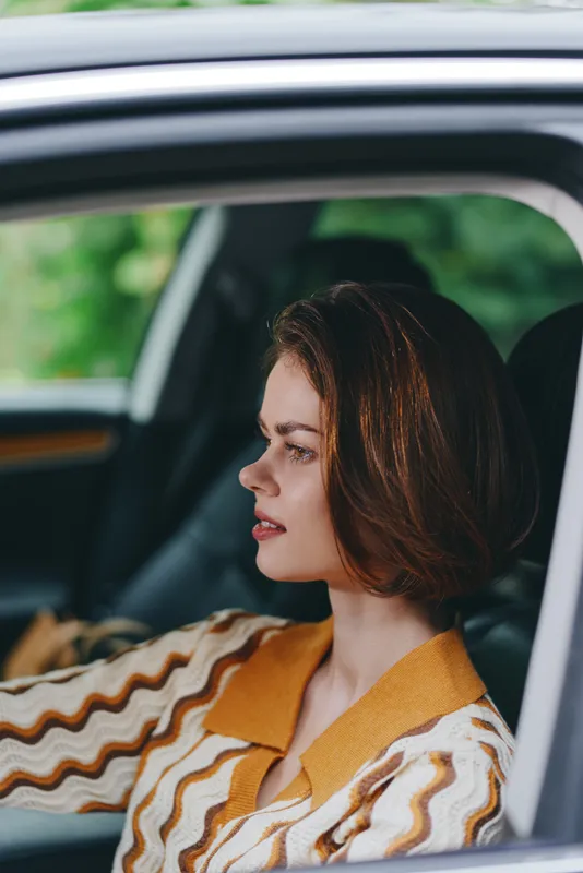 Portrait of a woman driving a car, side profile visible, calm expression, soft natural light, warm tones, casual fashion.