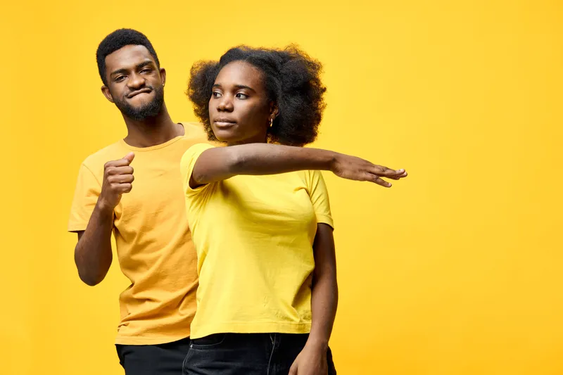 Young couple in matching yellow shirts expressing joy and playfulness against a bright yellow background, capturing a moment of happiness and connection