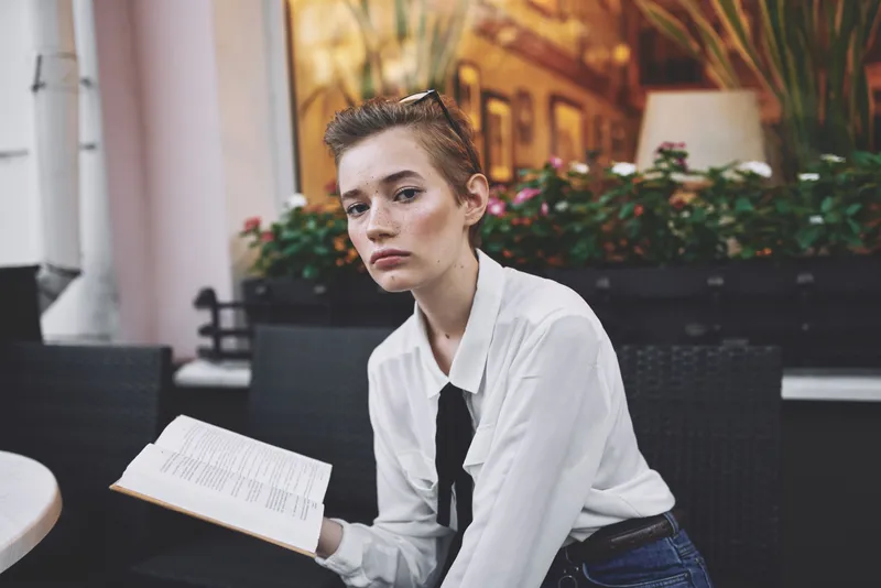 Коротко стриженная женщина держит в руках книгу и читает