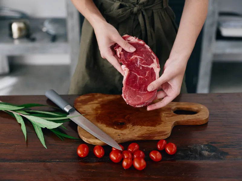 Женщина с ножом в руке нарезает свежее мясо стейка для жарки на кухне