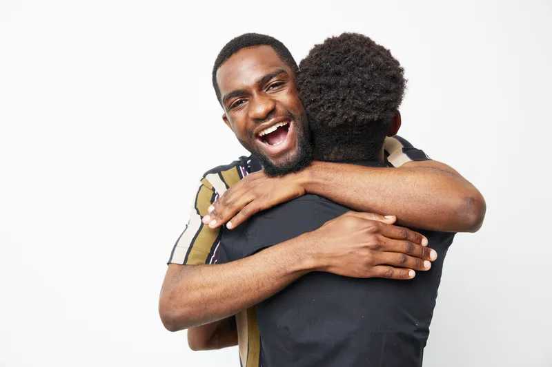 Happy black man embracing a friend, showcasing joy and friendship with a warm smile and expressive energy. A celebration of connection and mutual support.