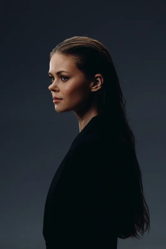Profile of a serious woman with long dark hair against dark background, showing contemplation and calm expression.