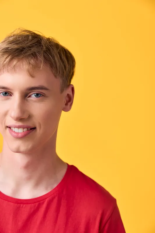 Smiling young man in a red shirt posing against a bright yellow background, casual studio setting, clean contemporary image for lifestyle, youth fashion, and upbeat branding visuals.