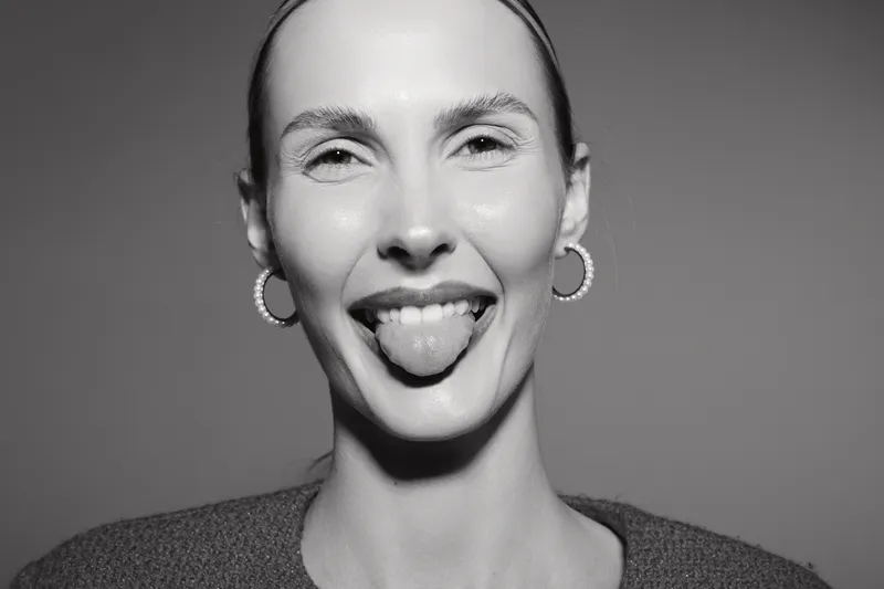 Smiling caucasian woman with light skin and earrings shows playful mood by sticking out tongue in close-up portrait. Concept for joy, fun, and positive facial expression.