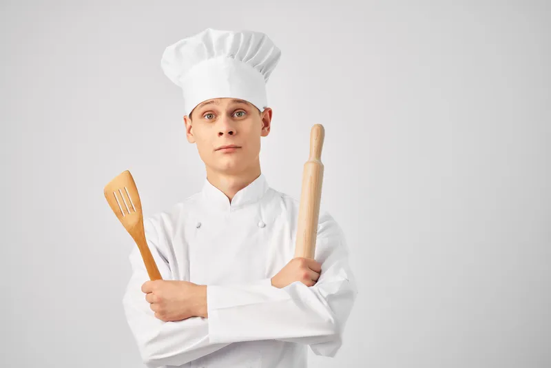 Повар-мужчина с кухонной утварью профессионально работает на светлом фоне