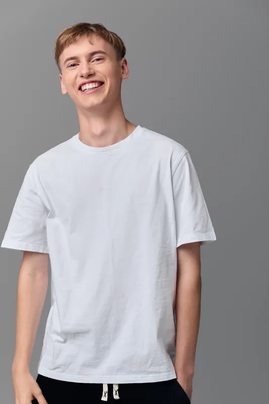 Smiling man in a white t shirt stands in a studio, casual and approachable, conveying friendly charm and youthful energy, clean background, minimal styling for versatile stock use