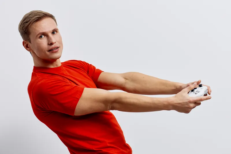Young man in red t-shirt holding gaming controller, casual pose, focused expression, isolated on plain white background, studio shot, lifestyle concept, entertainment, leisure, electronics, teenager s