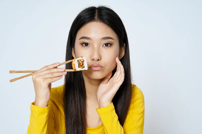 Женщина с палочками для еды возле рта, суши-роллы, морепродукты, диета, азиатская внешность