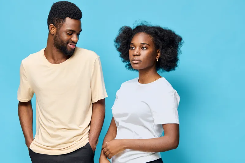 A stylish African couple in pastel t shirts against a vibrant blue background, expressing playful emotions and showcasing modern casual fashion