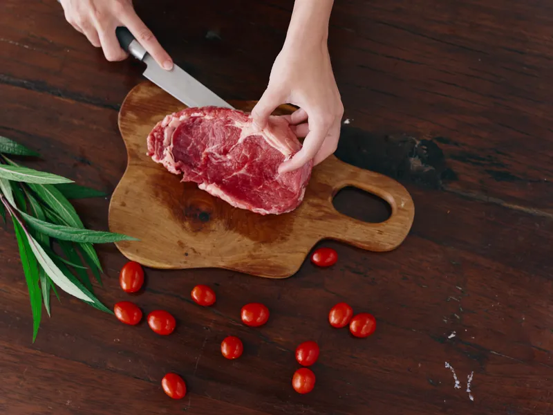 Женщина с ножом в руке нарезает свежее мясо для жарки на кухне