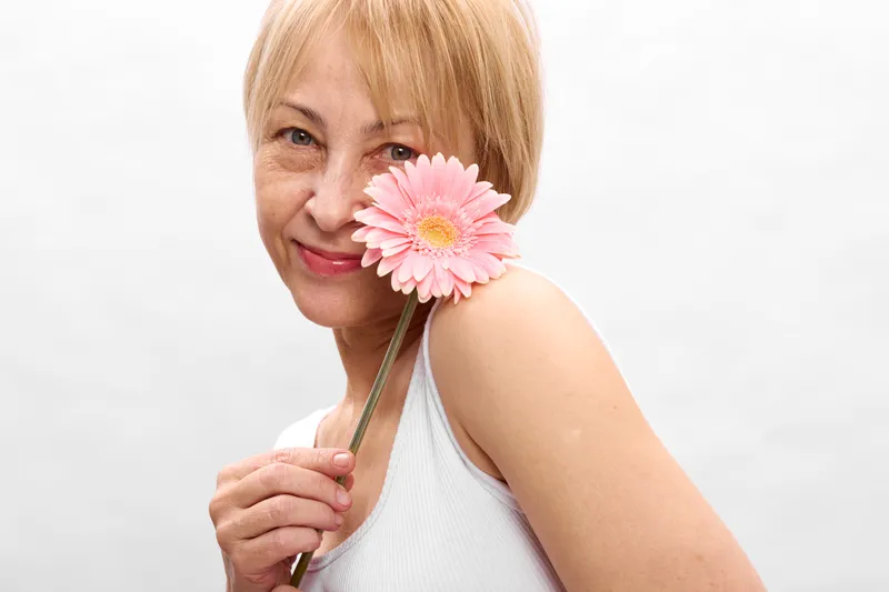 Woman portrait smiling with a pink flower, soft studio light, and clean white background, close up upper body, calm elegant mood, spring beauty, gentle serenity today