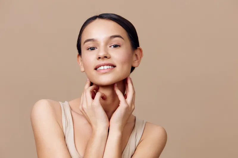 Young woman with natural beauty posing against a soft beige background, showcasing a serene expression and elegant style, embodying healthy skin and confidence
