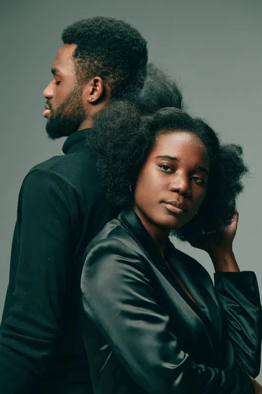 Two stylish models exuding confidence, showcasing natural hair, with contrasting black attire, against a muted gray background