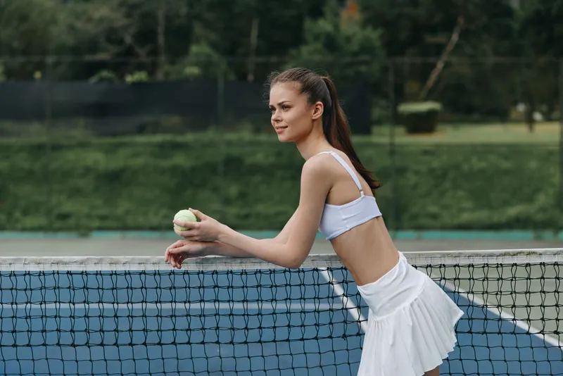 Young female tennis player in sporty outfit holding a tennis ball on a court, showcasing determination and focus against a green background