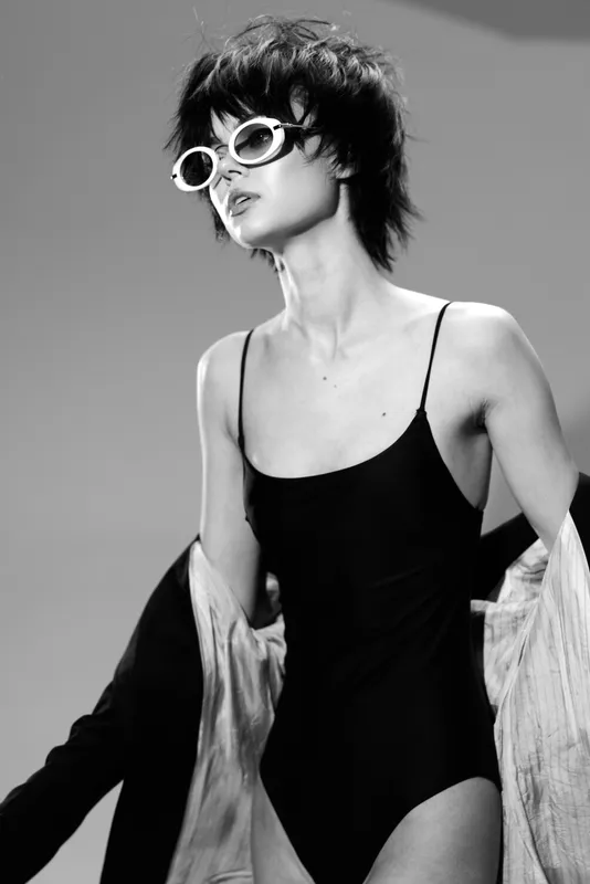 Stylish woman wearing sunglasses and a black bodysuit with a confident attitude in a black and white studio setting